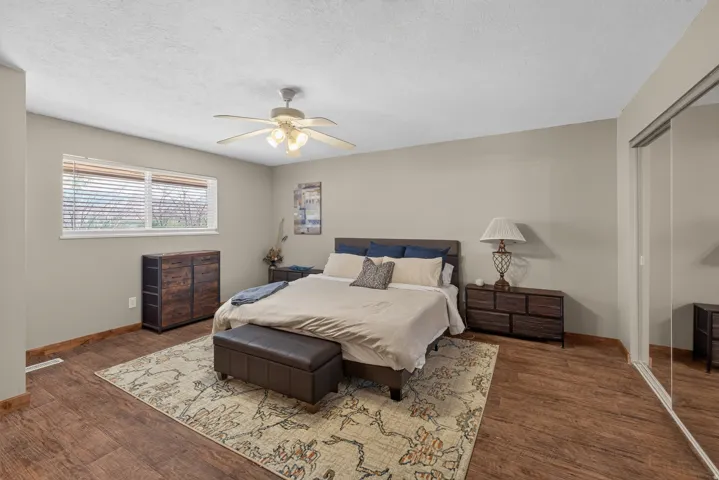 Spacious room featuring wood-finish flooring, a ceiling fan, and a large window with blinds