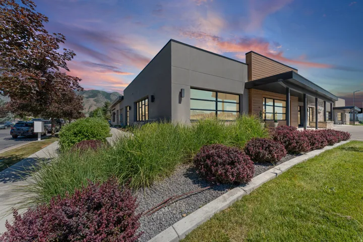 Modern commercial building featuring a gray stucco exterior, horizontal wood paneling, and large picture windows
