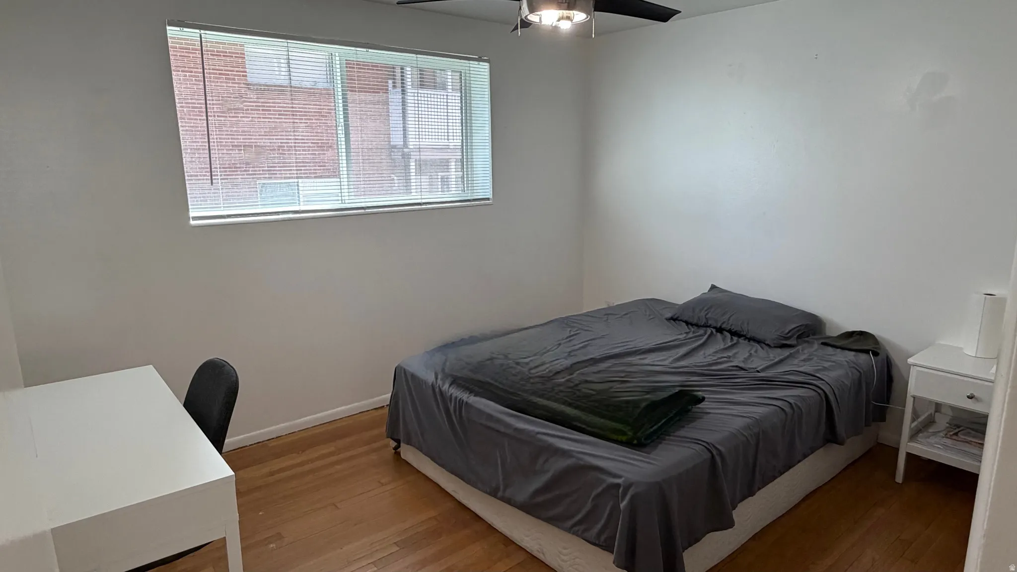Bedroom featuring wood floors, a ceiling fan with integrated lighting, and a window with horizontal blinds