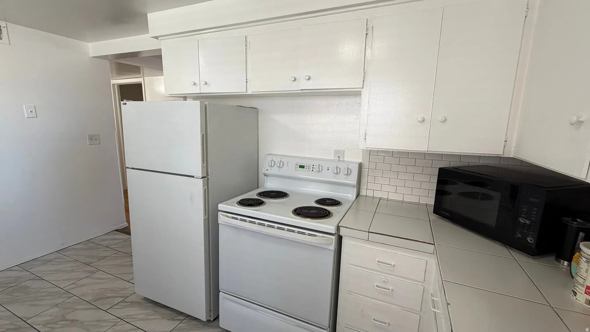 Kitchen featuring white cabinetry and appliances and tile flooring
