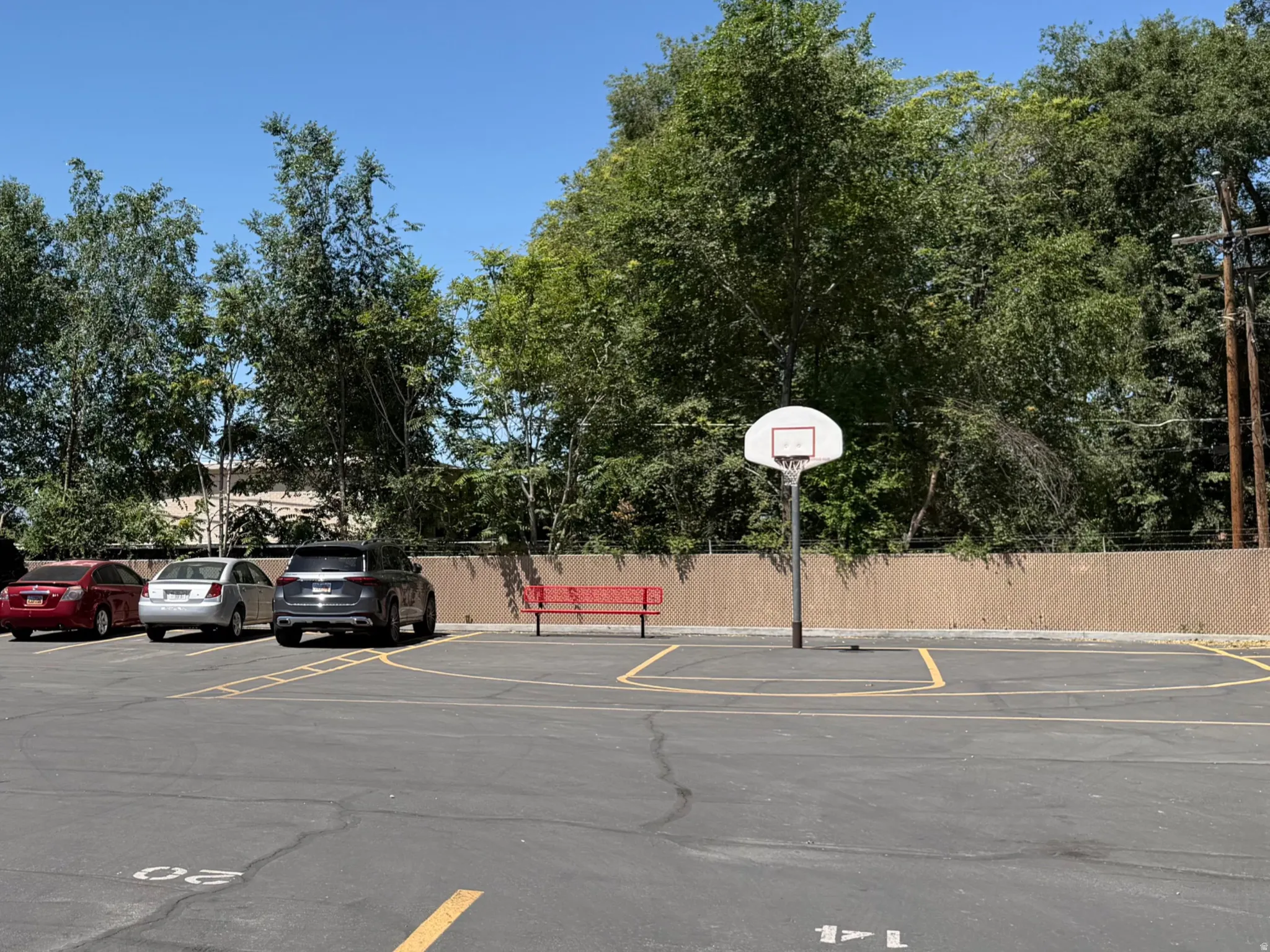Paved parking area featuring a basketball hoop and perimeter fencing