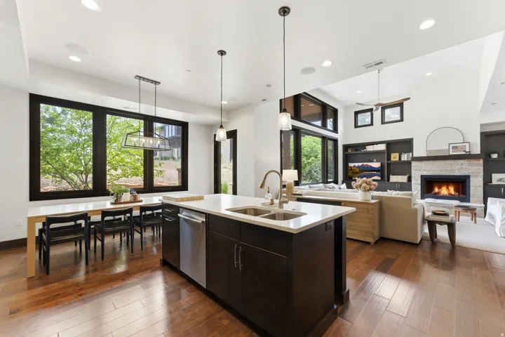 Open-concept living space featuring wood-finish flooring, a kitchen island with dual sinks, a built-in fireplace with stone surround, and an integrated entertainment unit with shelving