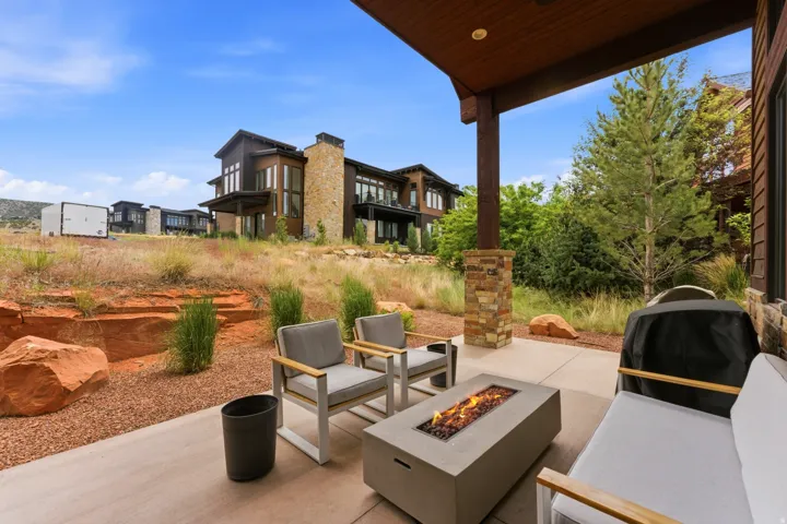 Expansive covered patio featuring a built-in fire pit, concrete flooring, and stone-clad support pillars