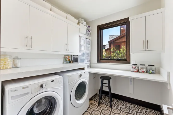 Dedicated utility space featuring white cabinetry with brushed nickel hardware, solid surface countertops, a dark wood-framed window, and patterned tile flooring