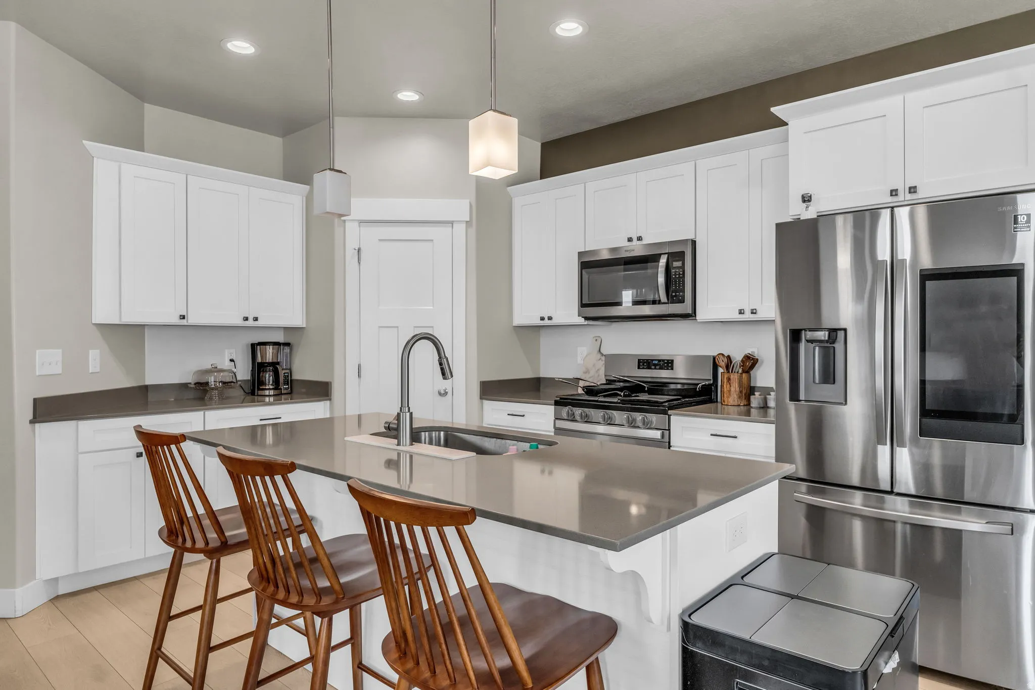 Modern kitchen featuring an island with a stainless steel sink, white shaker cabinetry, stainless steel appliances, and light wood-finish flooring