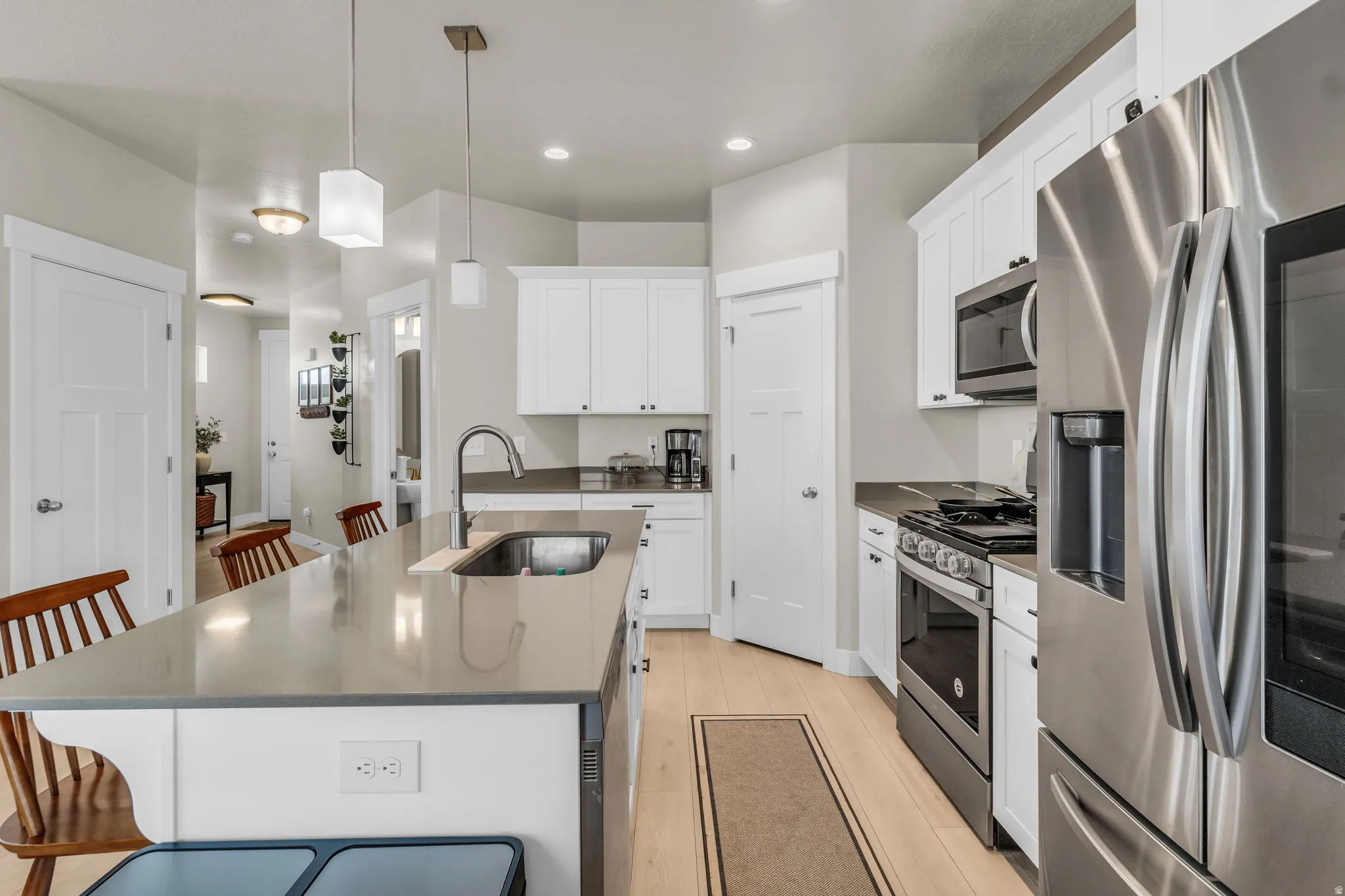 Kitchen featuring a large central island with an undermount sink, white cabinetry, light wood-finish flooring, stainless steel appliances, and pendant lighting