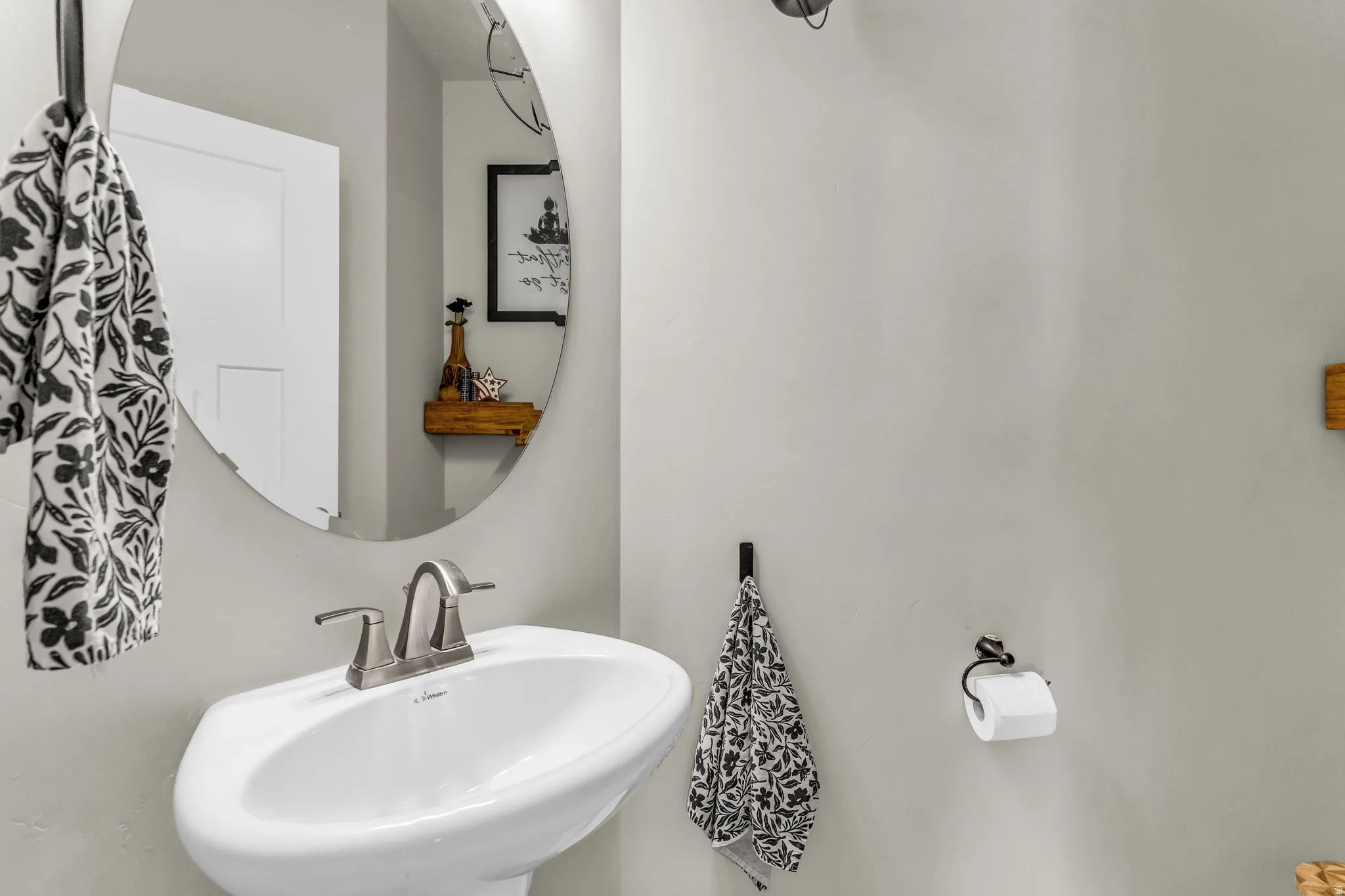 Pedestal sink with brushed nickel faucet, large oval mirror, and light gray walls