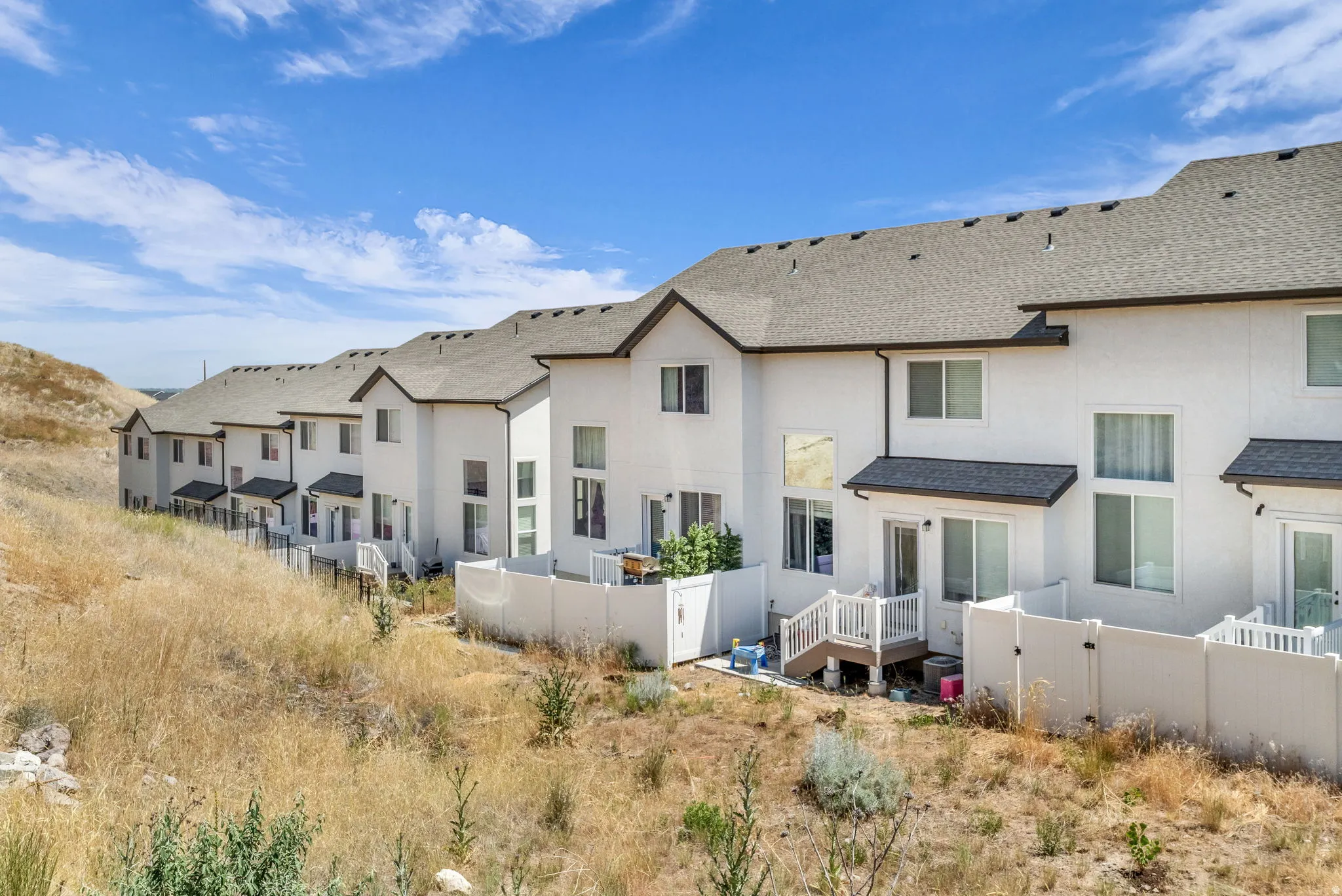 Rear elevations of multi-story townhomes featuring white stucco exteriors, gray shingle roofs, and individual private patios with white privacy fencing
