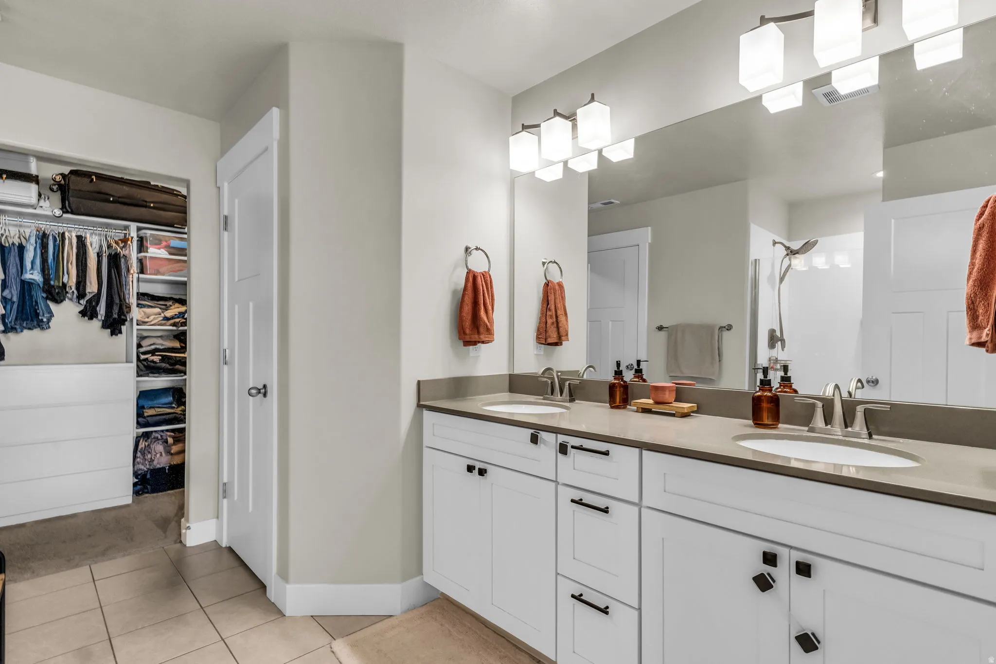 Double vanity featuring white shaker cabinetry, dark hardware, and light-toned countertops