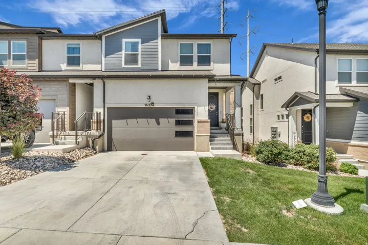 Contemporary townhome exterior featuring a two-tone facade, attached garage with frosted glass panels, concrete driveway, and front entry stairs with handrails