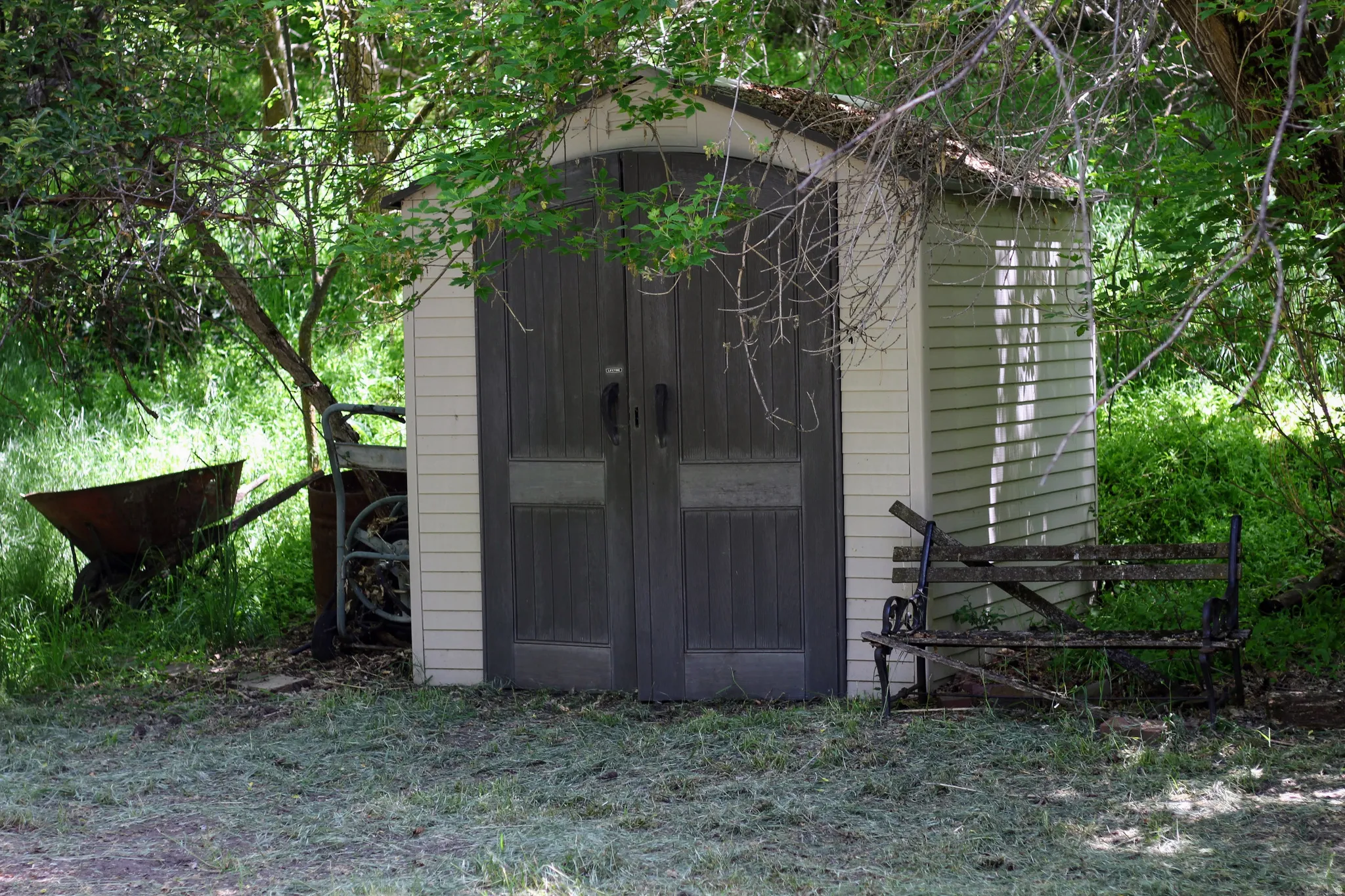 Detached storage shed featuring vertical panel doors, horizontal siding, and a sloped roofline