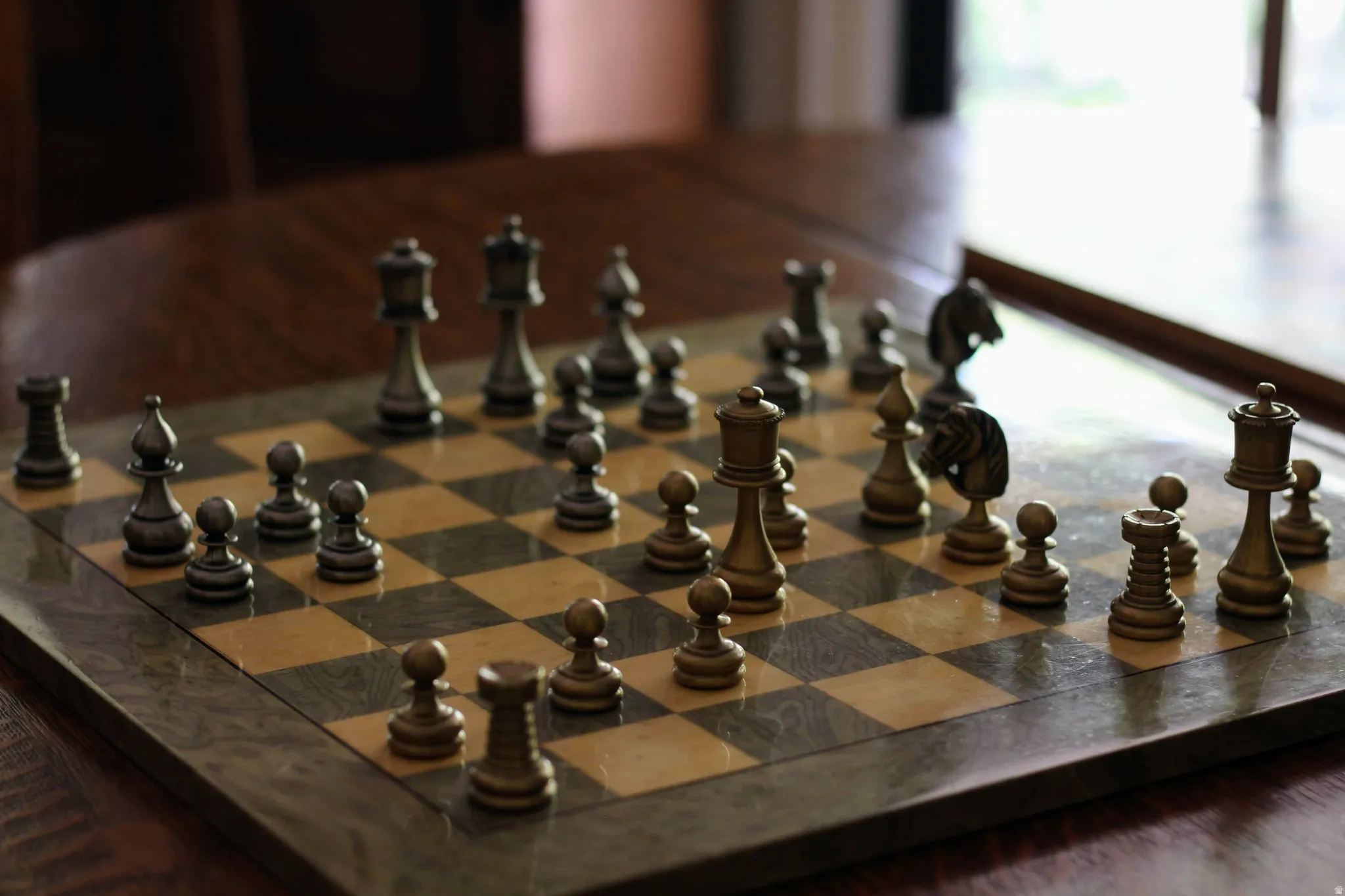 Stone chessboard with metal chess pieces resting on a dark wood-finish table