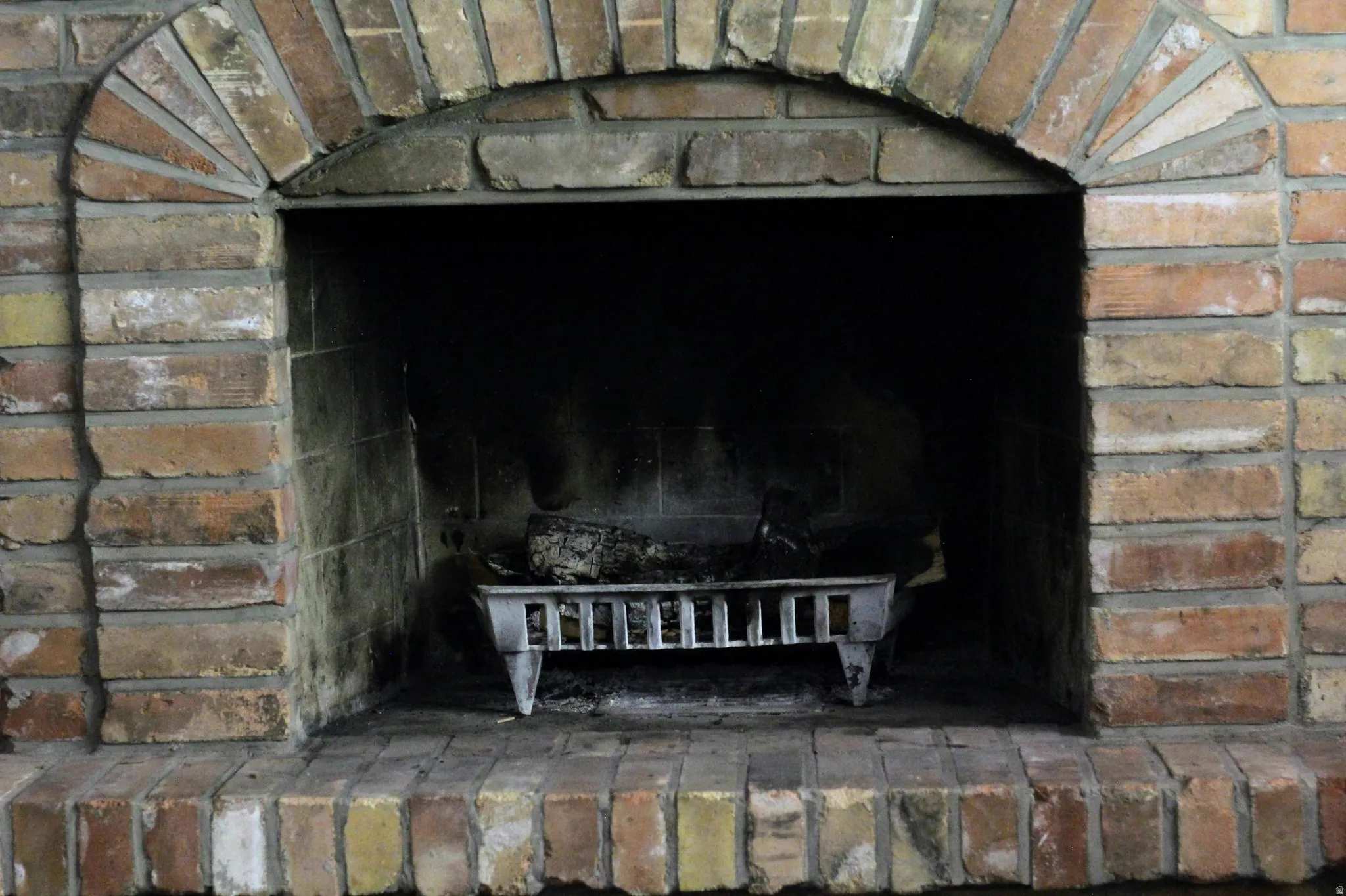Brick fireplace featuring an arched opening, a brick hearth, and a metal fire grate