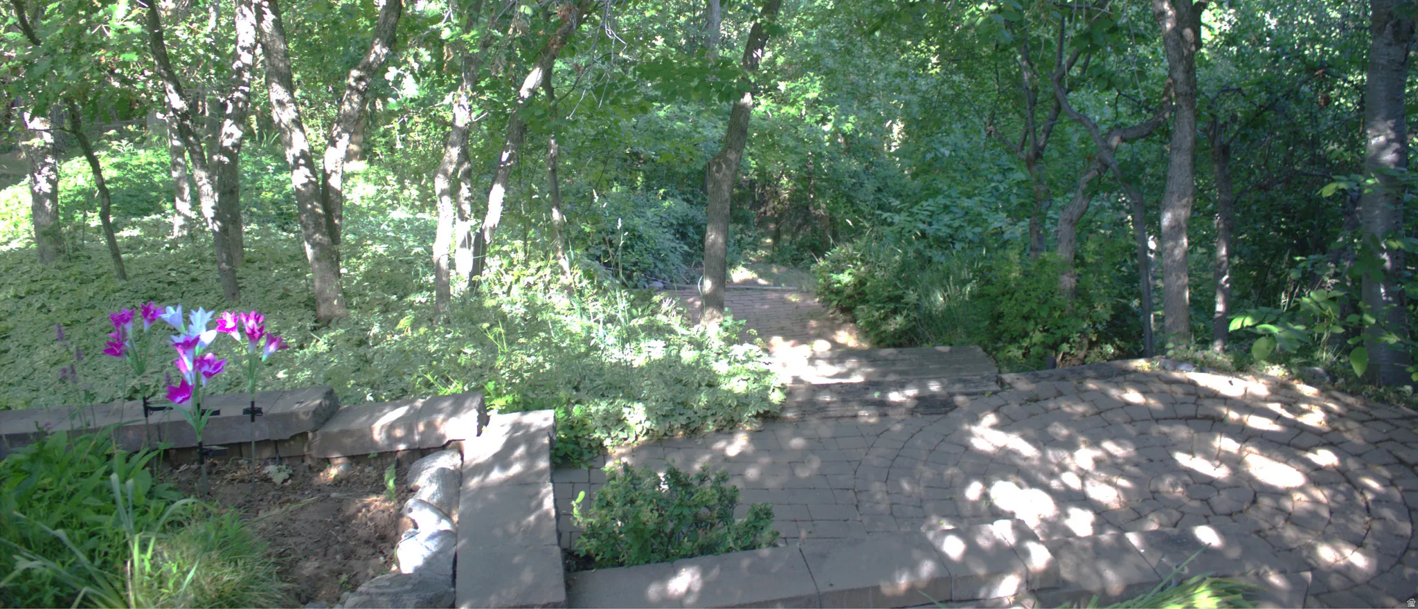 Tiered landscaping with natural stone pavers, a planting bed, and mature trees providing natural shading