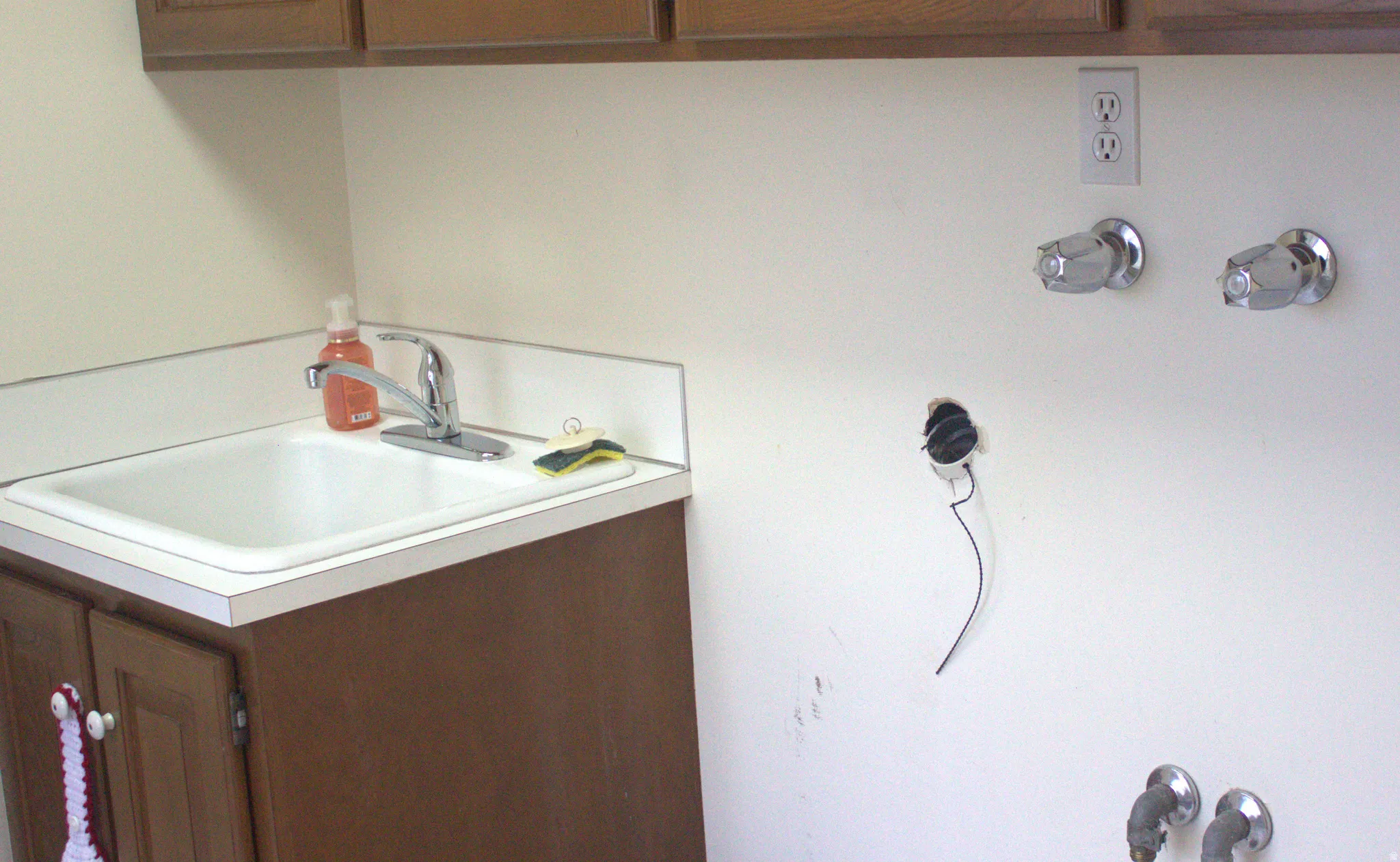 Utility sink with chrome faucet and white laminate countertop, accompanied by wood-finish cabinetry
