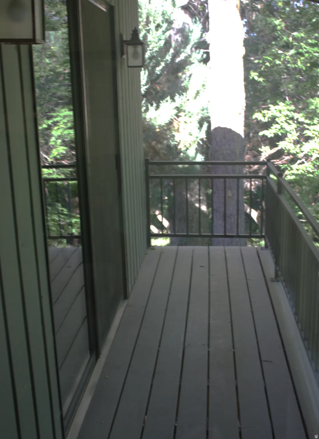 Exterior balcony featuring dark composite decking, black metal railings, and a sliding glass door