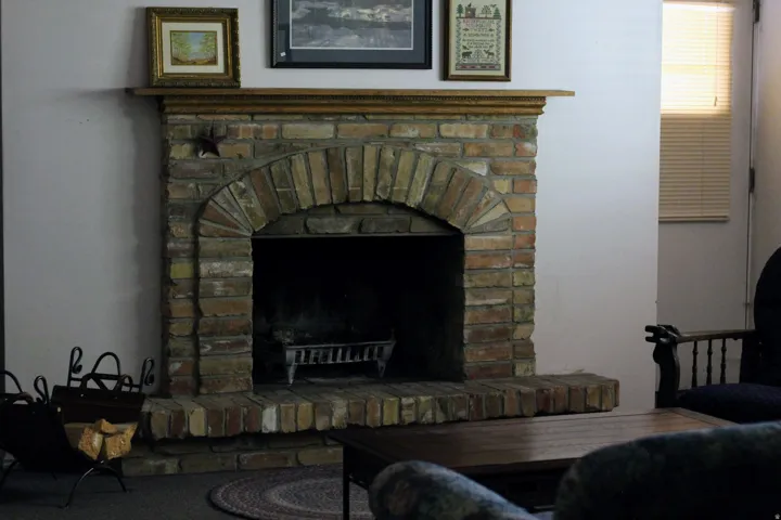 Brick fireplace featuring an arched firebox opening and a natural wood mantel