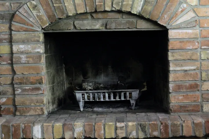Brick fireplace featuring an arched opening, a brick hearth, and a metal fire grate