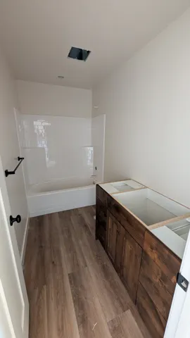 Contemporary bathroom featuring wood-finish flooring, a white subway tile tub surround, and a dark wood vanity base