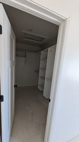 Walk-in closet featuring built-in shelving, hanging rods, and light-toned tile flooring