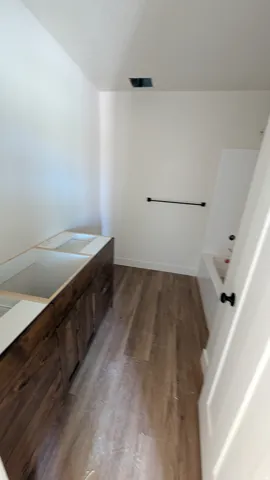 Spacious room featuring wood-finish flooring, a long wood-finish vanity base with multiple cabinets, and a white interior door with black hardware