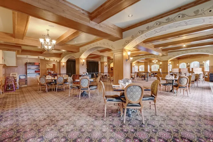 Spacious interior featuring exposed wooden beams, patterned carpeting, and decorative wall sconces