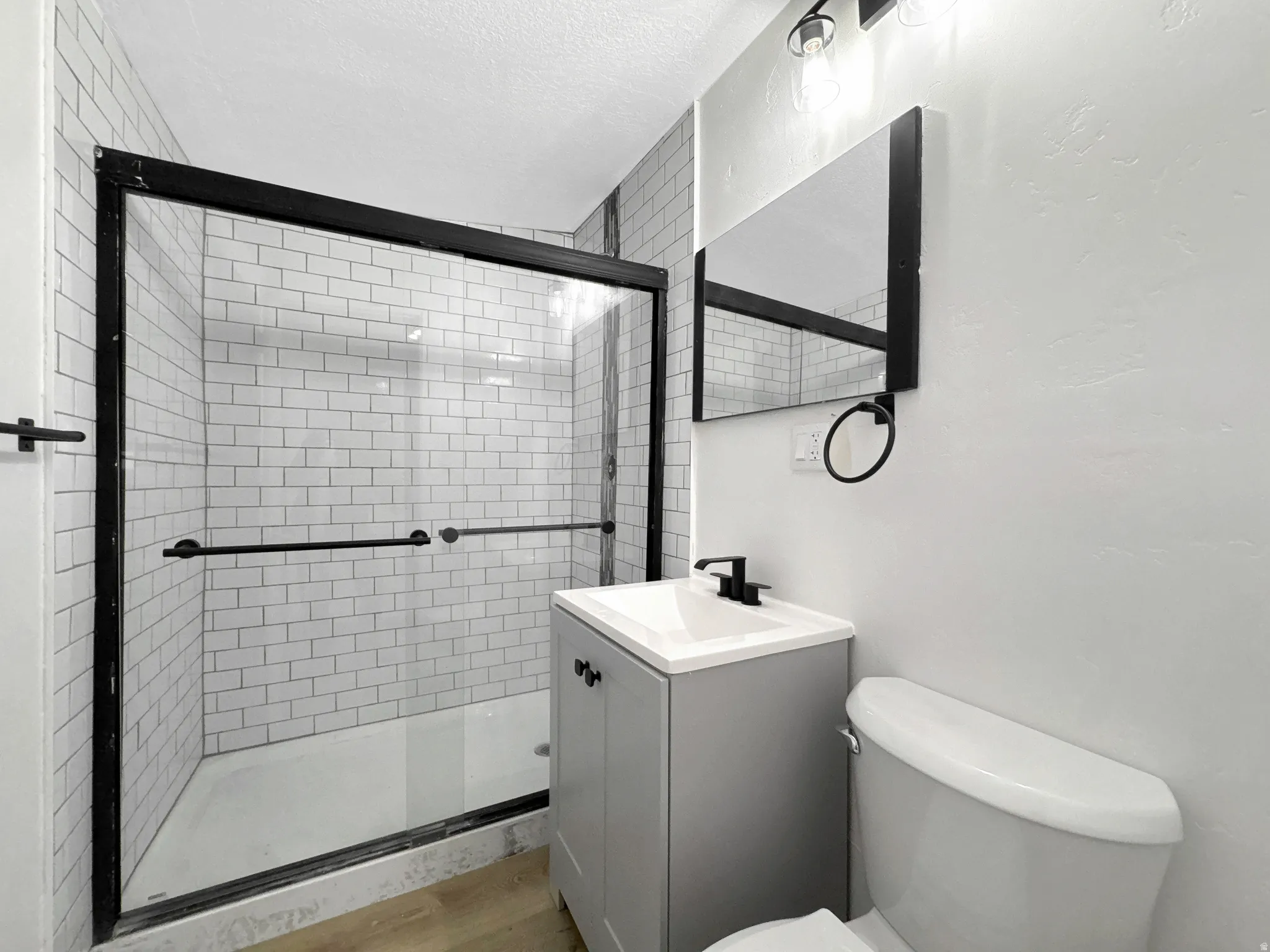 Bathroom featuring a shower with white subway tile surround and black-framed glass enclosure, a vanity with integrated sink and black faucet, and wood-finish flooring.  in detached ADU