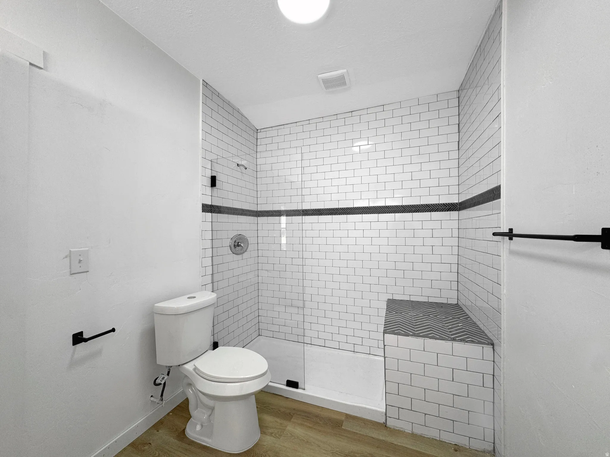 Shower enclosure featuring subway tile surround with a decorative accent band and integrated bench seating