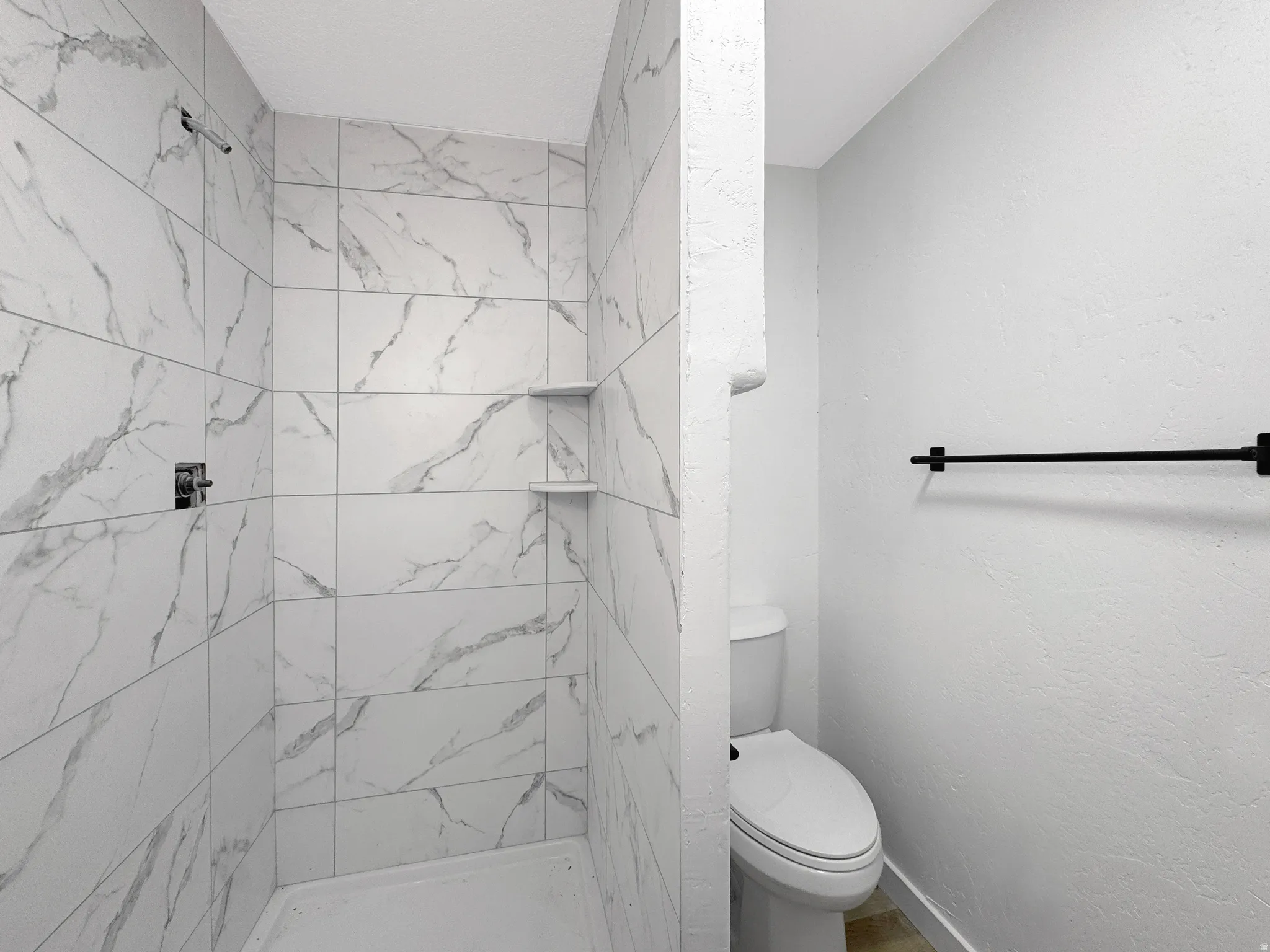 Walk-in shower with large format, marbled tile walls, integrated shelving, and a chrome shower fixture