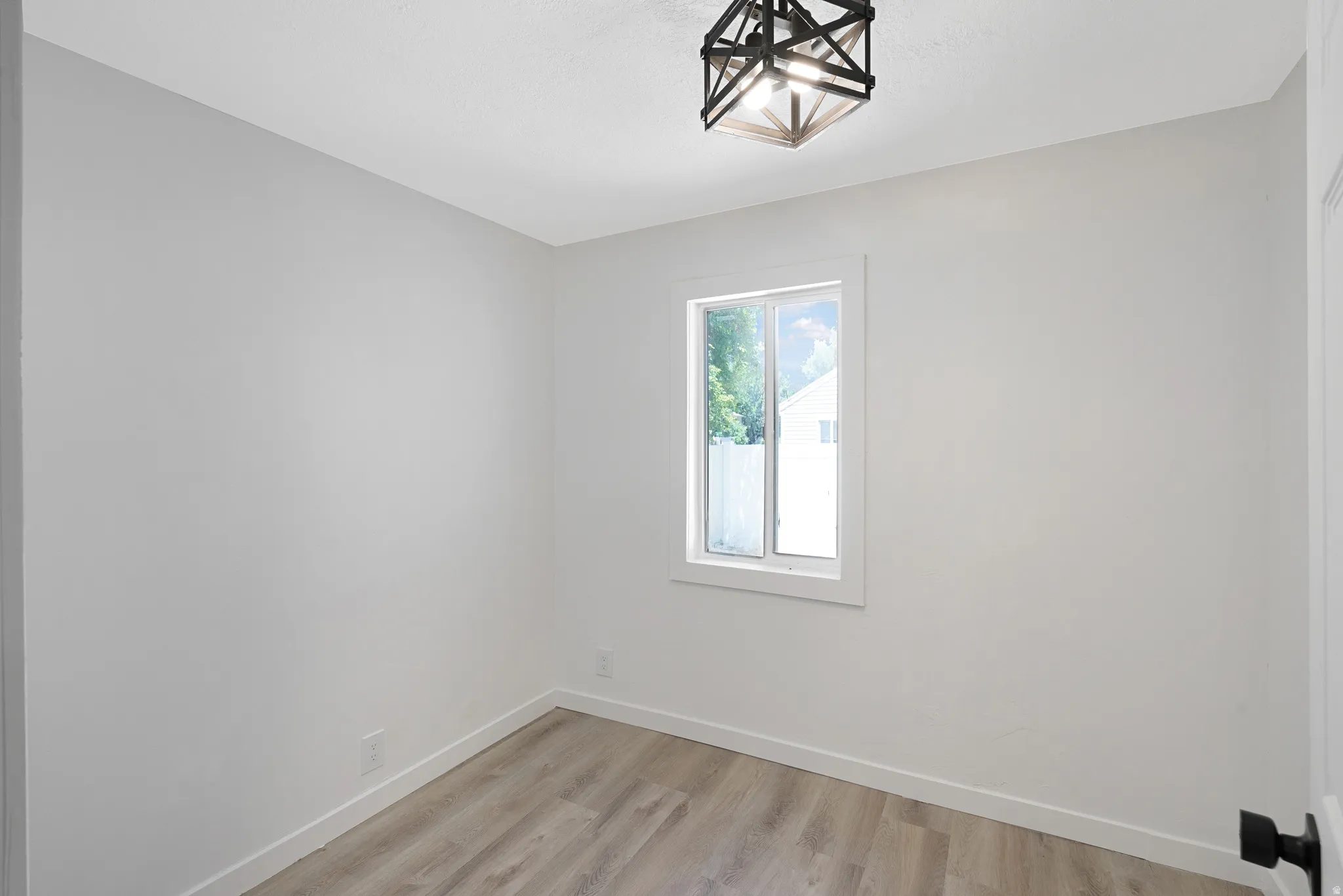 Interior room featuring a single window, overhead semi-flush mount lighting, light wood-finish flooring, white baseboards, and neutral wall paint