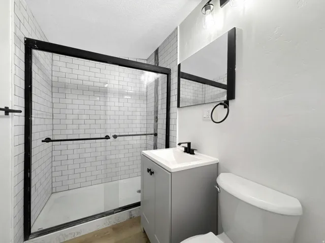 Bathroom featuring a shower with white subway tile surround and black-framed glass enclosure, a vanity with integrated sink and black faucet, and wood-finish flooring.  in detached ADU