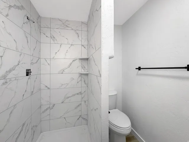 Walk-in shower with large format, marbled tile walls, integrated shelving, and a chrome shower fixture
