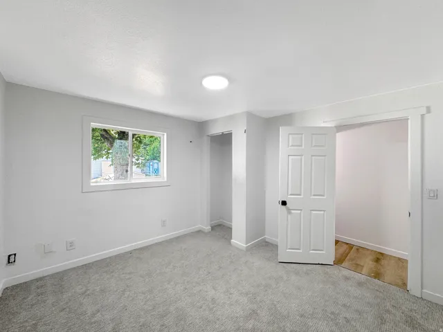 Spacious room featuring light gray carpeting, a single window with white trim, a built-in closet, a white panel door, and an overhead flush-mount light fixture