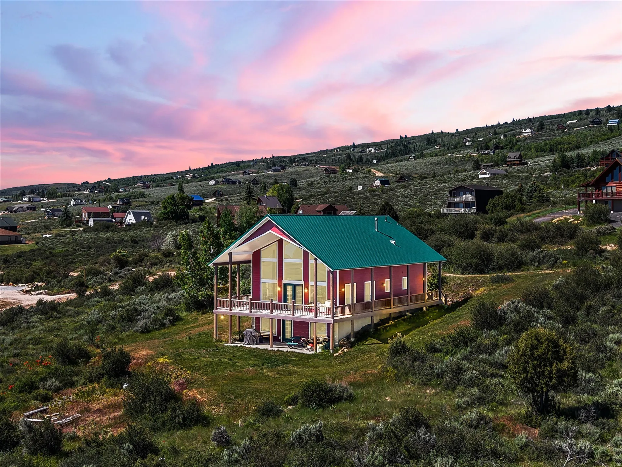 Modern architectural style property featuring a vibrant green metal roof, a full-length upper deck with wood railings, and a lower-level patio
