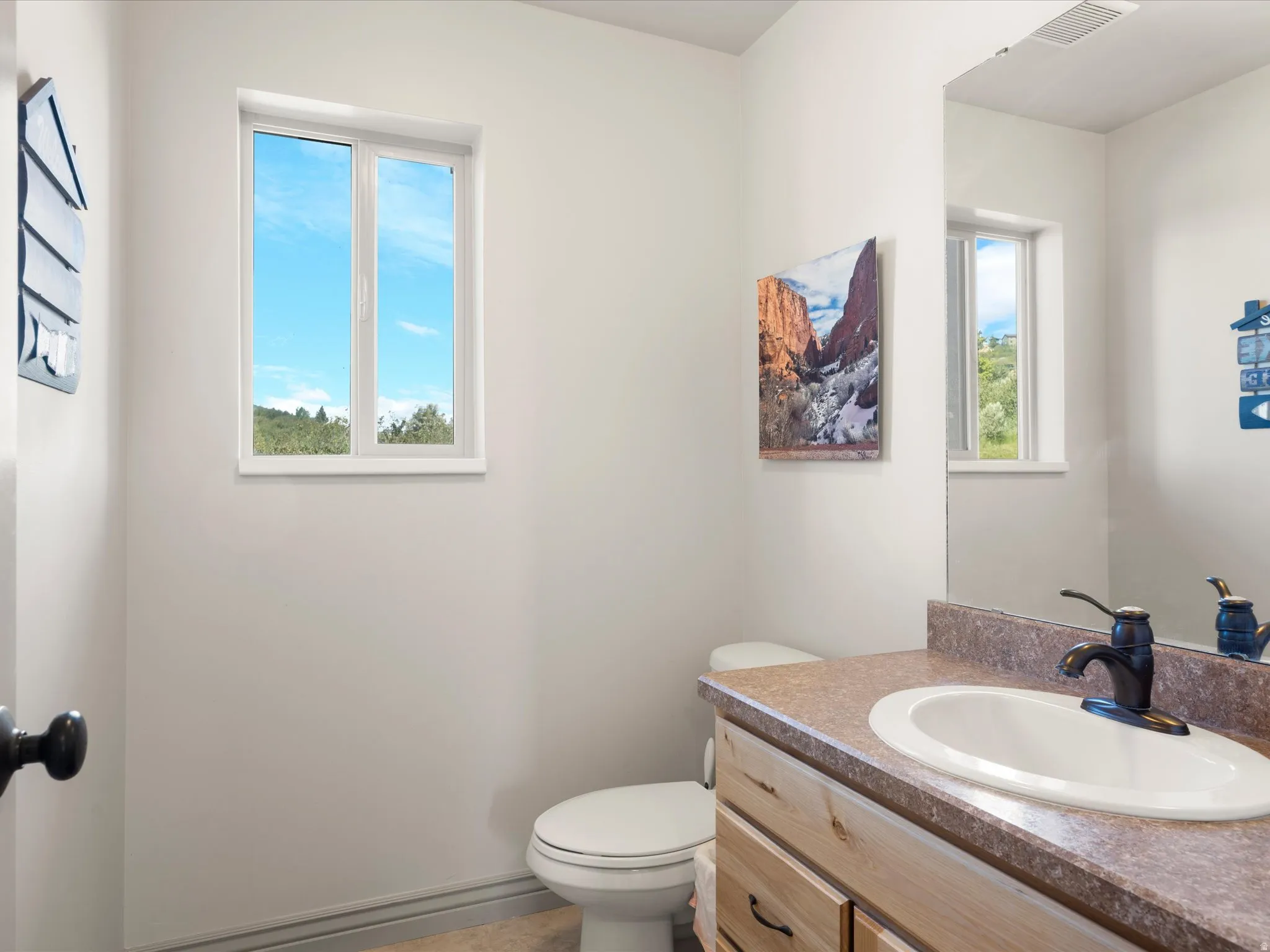 Bathroom featuring a single-pane window, vanity with a laminate countertop, undermount sink, and dark bronze faucet