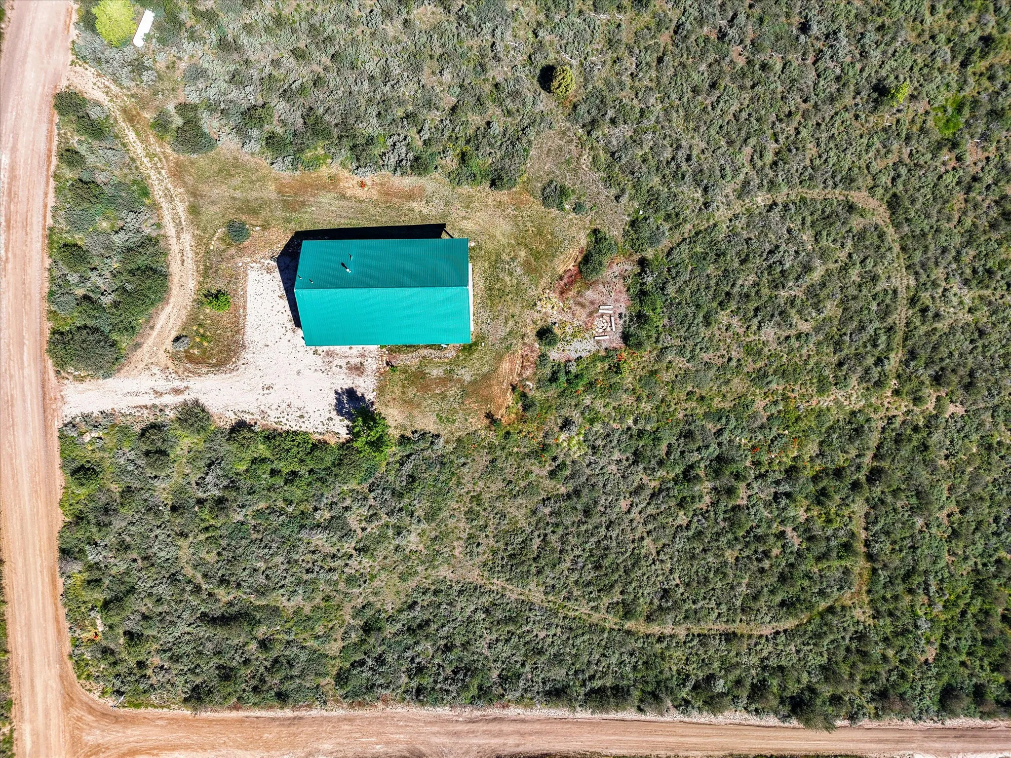 Expansive property featuring a green-roofed structure, gravel driveway, and surrounding natural vegetation