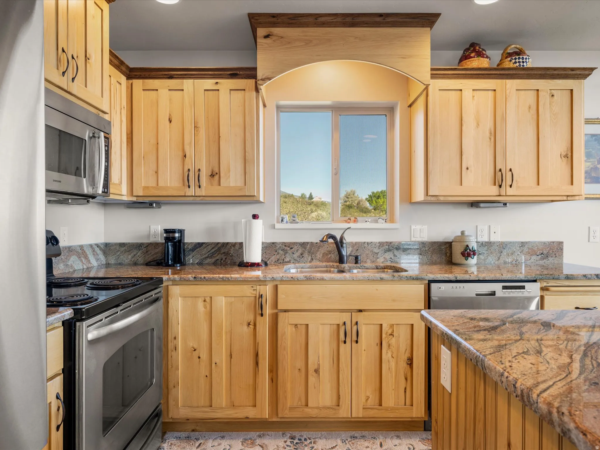 Kitchen featuring natural wood cabinetry, granite countertops, stainless steel appliances, a kitchen island, and a window above the sink