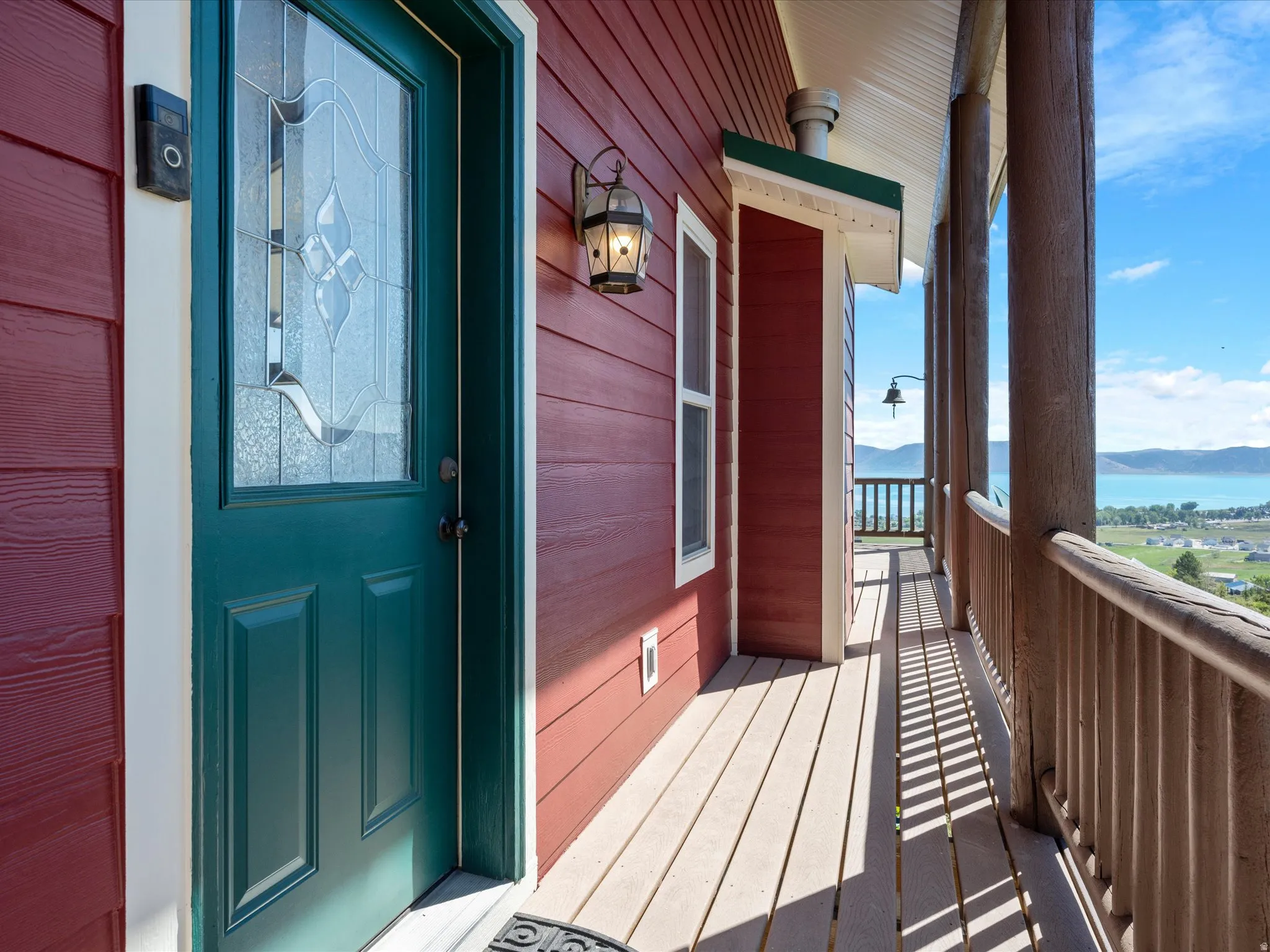 Inviting front entrance with a teal door featuring decorative leaded glass, complemented by red horizontal siding and a wall-mounted light fixture