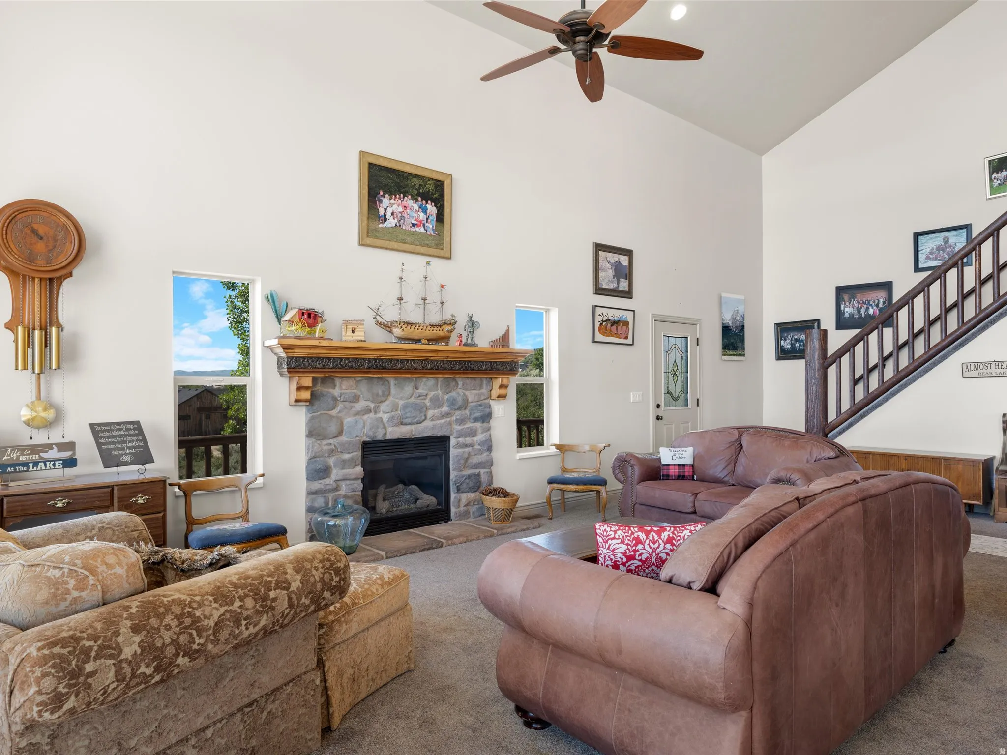 Living area featuring a stone fireplace with a decorative wood mantel, vaulted ceiling with a ceiling fan, and multiple windows