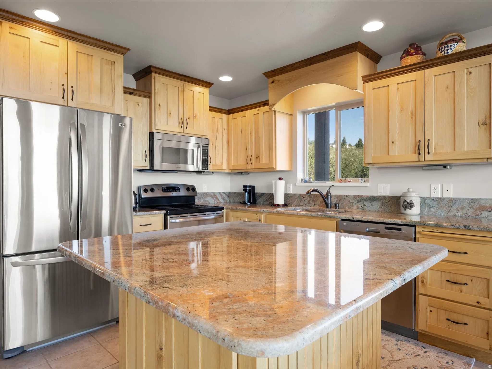 Kitchen featuring a central island with a polished stone countertop, light wood cabinetry, stainless steel appliances, recessed lighting, and a window above the sink