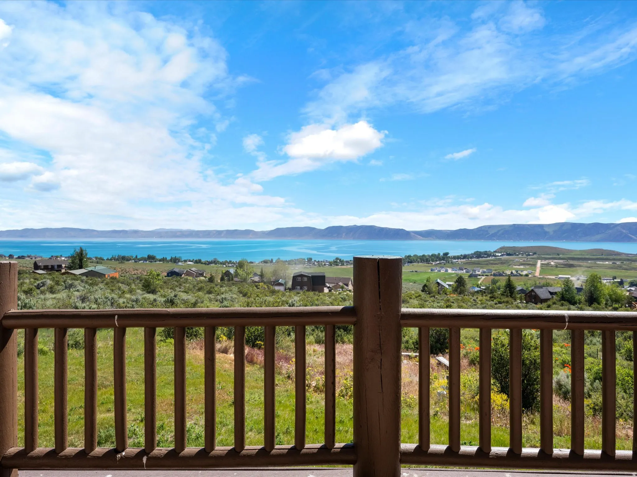 Expansive water body and distant mountain ranges with a foreground featuring a wooden balcony railing and a verdant landscape