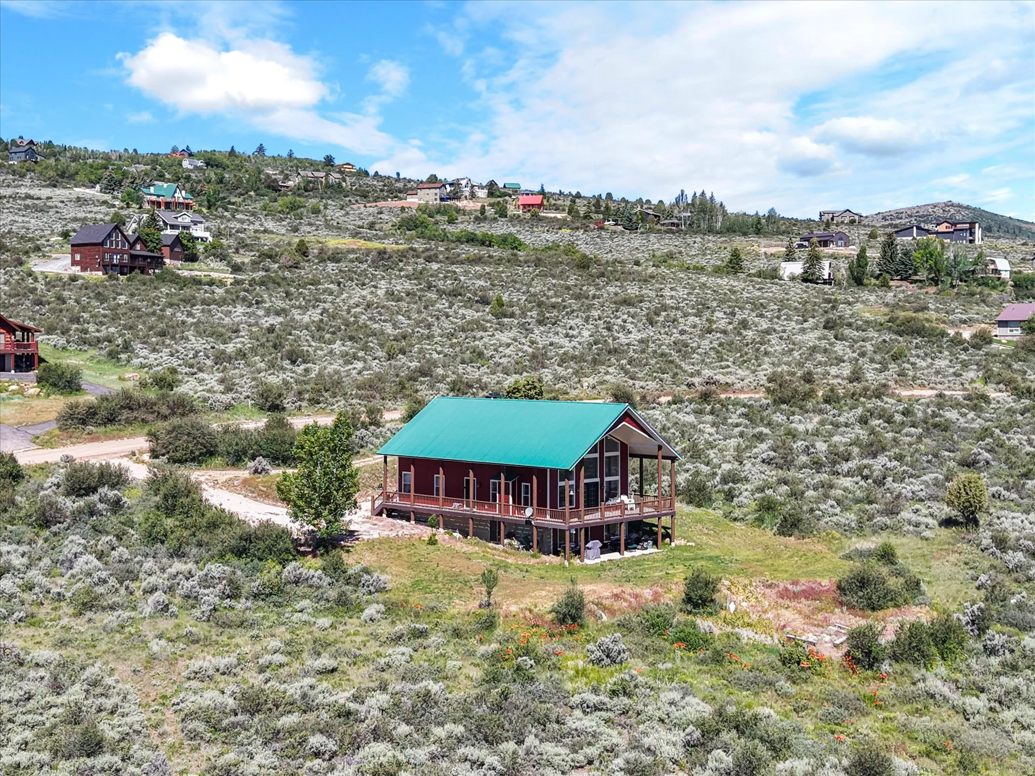 Hillside cabin featuring a vibrant green metal roof, red exterior siding, and a spacious wrap-around deck