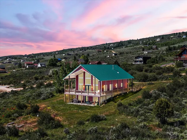 Modern architectural style property featuring a vibrant green metal roof, a full-length upper deck with wood railings, and a lower-level patio