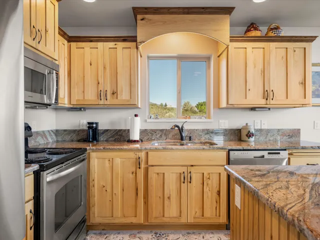 Kitchen featuring natural wood cabinetry, granite countertops, stainless steel appliances, a kitchen island, and a window above the sink