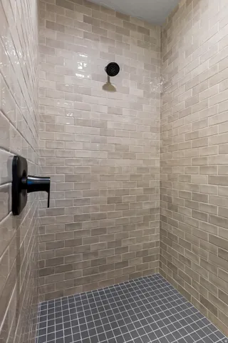Shower stall featuring light gray subway tile walls and dark gray square tile flooring