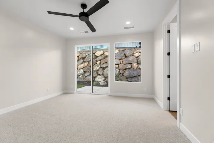 Recessed lighting and a matte black ceiling fan illuminate this carpeted room, featuring a sliding glass door and an additional window