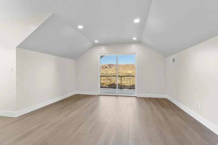 Open room with light wood-finish flooring, white walls, and a vaulted ceiling with recessed lighting