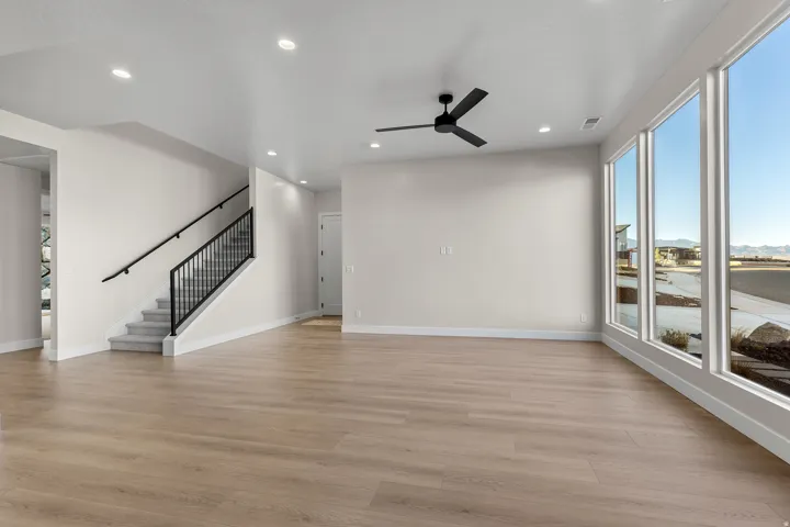 Spacious living area featuring light wood-finish flooring, a modern black ceiling fan, and recessed lighting