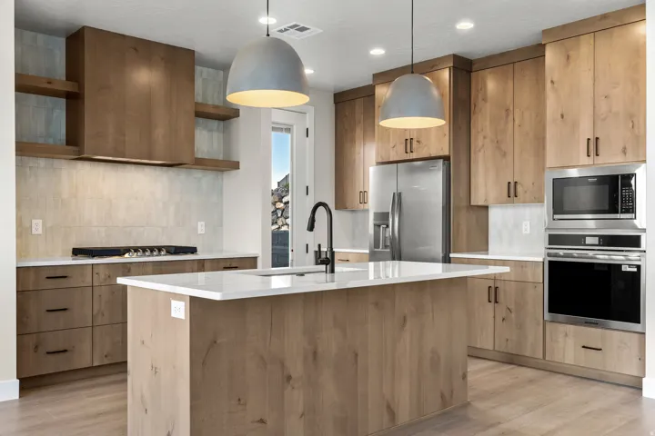 Spacious kitchen featuring wood-finish cabinetry, quartz countertops, a large center island with a sink, stainless steel appliances, and wood-finish flooring