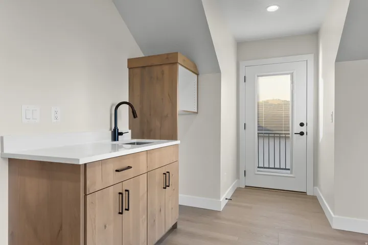 Light wood-finish cabinetry with black hardware, white countertop, and a black gooseneck faucet